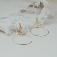 Load image into Gallery viewer, Gold dangling earrings made of two uneven thin circles of sterling silver placed on a table.
